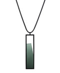 The Lucia necklace in Cypress Green features a sleek rectangular pendant that emphasizes form and material. A cast resin element rests within a black frame, creating a sense of depth and quiet luminosity. The elongated shape draws the eye, offering a refined balance between structure and softness. Minimal and striking, the Lucia necklace adds a sculptural accent that complements both everyday and statement looks.
