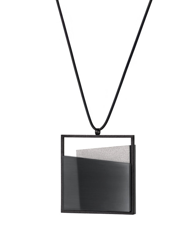 side view of the Mara necklace in ash grey evokes depth, stillness, and movement within form. Concrete is cast into resin inside a square frame, where the materials meet in a smooth, fluid line. The surface reflects light with quiet subtlety, creating the sense of horizon and depth. The Mara necklace embodies balance and serenity through modern, sculptural design.