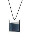 side view of the Mara necklace in cerulean blue resin evokes depth, stillness, and movement within form. Concrete is cast into resin inside a square frame, where the materials meet in a smooth, fluid line. The surface reflects light with quiet subtlety, creating the sense of horizon and depth. The Mara necklace embodies balance and serenity through modern, sculptural design.