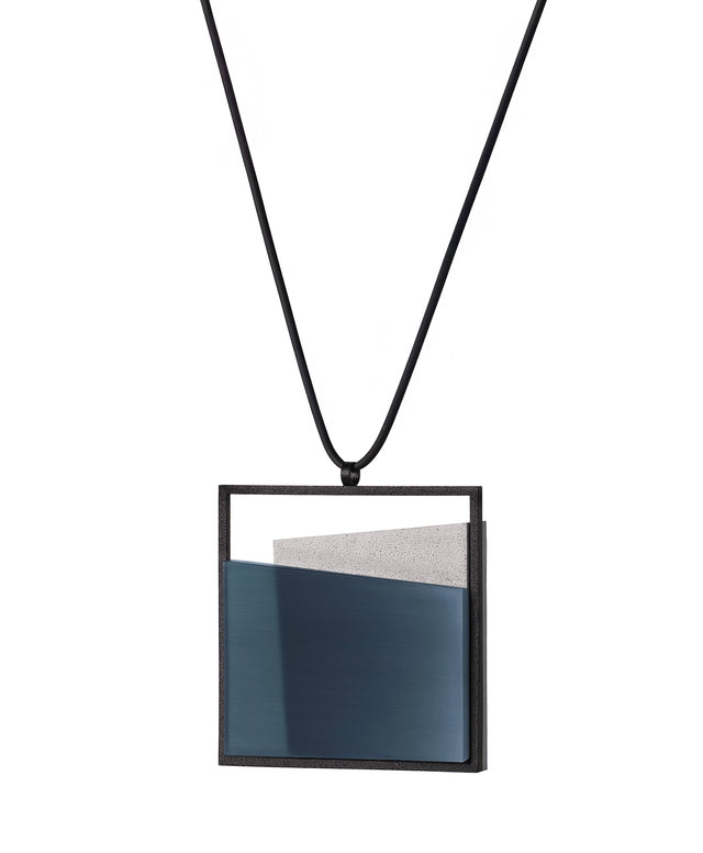 side view of the Mara necklace in cerulean blue resin evokes depth, stillness, and movement within form. Concrete is cast into resin inside a square frame, where the materials meet in a smooth, fluid line. The surface reflects light with quiet subtlety, creating the sense of horizon and depth. The Mara necklace embodies balance and serenity through modern, sculptural design.