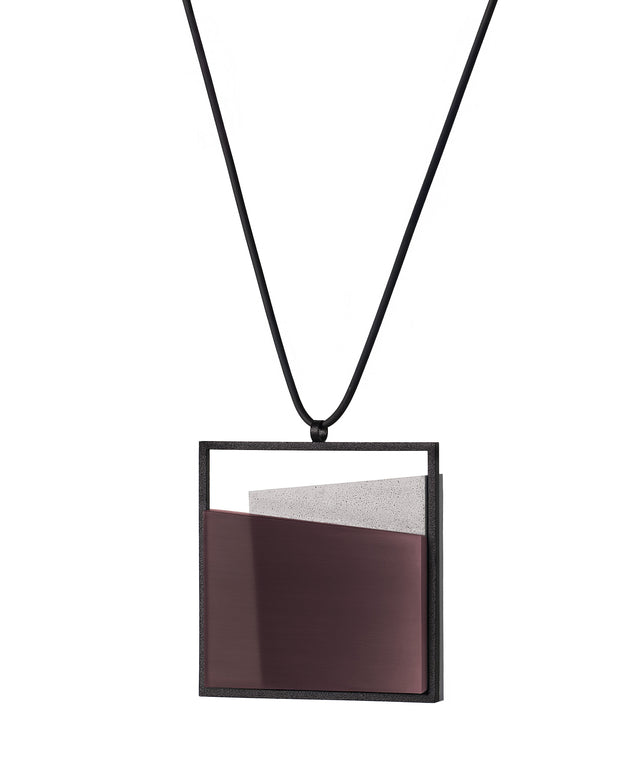 side view of The Mara necklace in cognac resin evokes depth, stillness, and movement within form. Concrete is cast into resin inside a square frame, where the materials meet in a smooth, fluid line. The surface reflects light with quiet subtlety, creating the sense of horizon and depth. The Mara necklace embodies balance and serenity through modern, sculptural design.