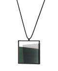 side view of The Mara necklace in  cypress green evokes stillness, and movement within form. Concrete is cast into resin inside a square frame, where the materials meet in a smooth, fluid line. The surface reflects light with quiet subtlety, creating the sense of horizon and depth. The Mara necklace embodies balance and serenity through modern, sculptural design.