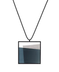 The Mara necklace in cerulean blue resin evokes depth, stillness, and movement within form. Concrete is cast into resin inside a square frame, where the materials meet in a smooth, fluid line. The surface reflects light with quiet subtlety, creating the sense of horizon and depth. The Mara necklace embodies balance and serenity through modern, sculptural design.
