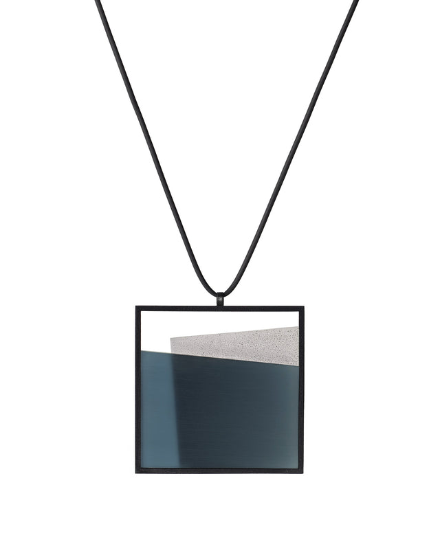The Mara necklace in cerulean blue resin evokes depth, stillness, and movement within form. Concrete is cast into resin inside a square frame, where the materials meet in a smooth, fluid line. The surface reflects light with quiet subtlety, creating the sense of horizon and depth. The Mara necklace embodies balance and serenity through modern, sculptural design.