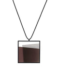The Mara necklace in cognac resin evokes depth, stillness, and movement within form. Concrete is cast into resin inside a square frame, where the materials meet in a smooth, fluid line. The surface reflects light with quiet subtlety, creating the sense of horizon and depth. The Mara necklace embodies balance and serenity through modern, sculptural design.