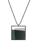 The Mara necklace in cypress green resin evokes depth, stillness, and movement within form. Concrete is cast into resin inside a square frame, where the materials meet in a smooth, fluid line. The surface reflects light with quiet subtlety, creating the sense of horizon and depth. The Mara necklace embodies balance and serenity through modern, sculptural design.