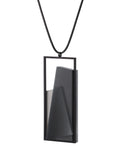 Side view of The Naia necklace in Ash grey embodies the feeling of wearing a work of art. Within its black rectangular frame, layers of resin and concrete are composed with sculptural precision, creating depth and quiet movement. The graduated tone of the resin shifts gently with the light, giving the piece a quiet, sculptural presence. Balanced and distinctive, the Naia necklace transforms simple geometry into a refined expression of wearable art.