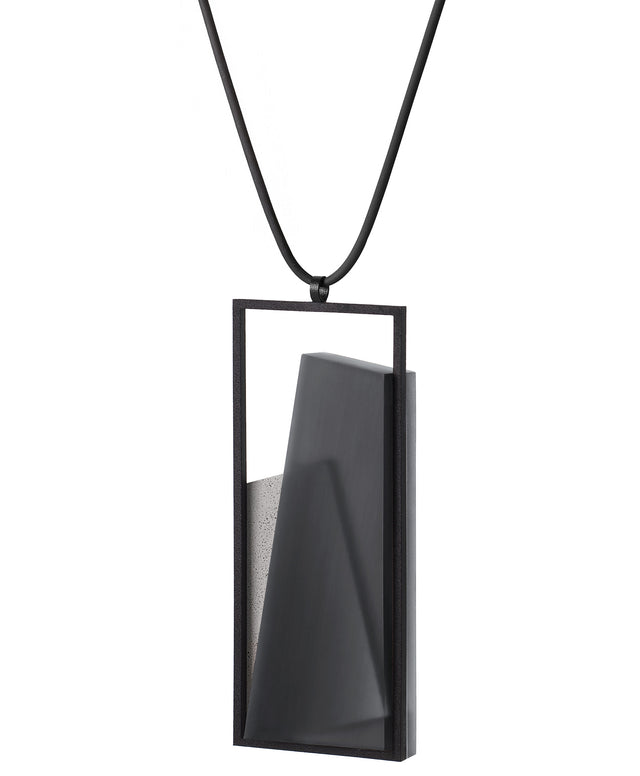 Side view of The Naia necklace in Ash grey embodies the feeling of wearing a work of art. Within its black rectangular frame, layers of resin and concrete are composed with sculptural precision, creating depth and quiet movement. The graduated tone of the resin shifts gently with the light, giving the piece a quiet, sculptural presence. Balanced and distinctive, the Naia necklace transforms simple geometry into a refined expression of wearable art.