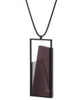 side view of The Naia necklace embodies the feeling of wearing a work of art. Within its black rectangular frame, layers of resin and concrete are composed with sculptural precision, creating depth and quiet movement. The graduated tone of the resin shifts gently with the light, giving the piece a quiet, sculptural presence. Balanced and distinctive, the Naia necklace transforms simple geometry into a refined expression of wearable art.