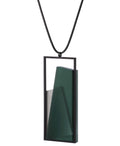 side view of the The Naia necklace in Cypress Green embodies the feeling of wearing a work of art. Within its black rectangular frame, layers of resin and concrete are composed with sculptural precision, creating depth and quiet movement. The graduated tone of the resin shifts gently with the light, giving the piece a quiet, sculptural presence. Balanced and distinctive, the Naia necklace transforms simple geometry into a refined expression of wearable art.