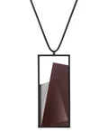 The Naia necklace embodies the feeling of wearing a work of art. Within its black rectangular frame, layers of resin and concrete are composed with sculptural precision, creating depth and quiet movement. The graduated tone of the resin shifts gently with the light, giving the piece a quiet, sculptural presence. Balanced and distinctive, the Naia necklace transforms simple geometry into a refined expression of wearable art.