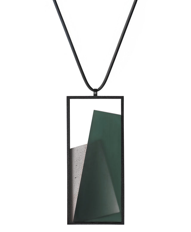 The Naia necklace in Cypress green embodies the feeling of wearing a work of art. Within its black rectangular frame, layers of resin and concrete are composed with sculptural precision, creating depth and quiet movement. The graduated tone of the resin shifts gently with the light, giving the piece a quiet, sculptural presence. Balanced and distinctive, the Naia necklace transforms simple geometry into a refined expression of wearable art.