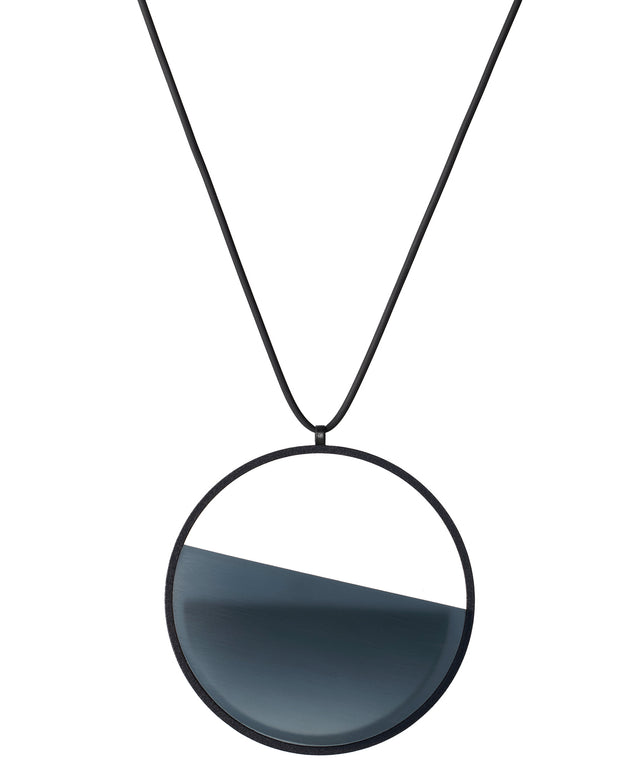 The Vestra necklace in cerulean blue resin embodies balance and quiet strength. Its name, derived from the Latin vestra, meaning “yours,” speaks to a personal connection between wearer and form. Within the circular frame, concrete is cast into resin revealing a smooth plane of depth and tone, reflecting light in a soft, fluid way. The composition feels calm and grounded, offering a sculptural presence that becomes uniquely individual when worn.