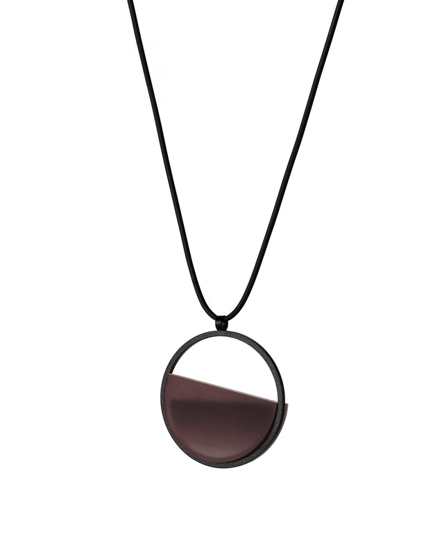 the side version of The Vestra Small necklace in cognac resin captures the same sense of balance and quiet strength in a more understated form that the larger version. Named from the Latin vestra, meaning “yours,” it reflects a personal connection between light, material, and wearer. The smaller circular frame holds a smooth resin plane with a cast concrete inset that reveals gentle depth and tone, creating a soft glow close to the body.