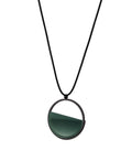 side version of the The Vestra Small necklace in cypress green resin captures the same sense of balance and quiet strength in a more understated form that the larger version. Named from the Latin vestra, meaning “yours,” it reflects a personal connection between light, material, and wearer. The smaller circular frame holds a smooth resin plane with a cast concrete inset that reveals gentle depth and tone, creating a soft glow close to the body.