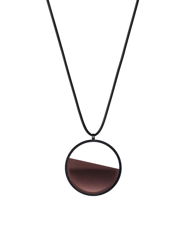 The Vestra Small necklace in cognac resin captures the same sense of balance and quiet strength in a more understated form that the larger version. Named from the Latin vestra, meaning “yours,” it reflects a personal connection between light, material, and wearer. The smaller circular frame holds a smooth resin plane with a cast concrete inset that reveals gentle depth and tone, creating a soft glow close to the body.