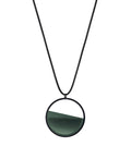 The Vestra Small necklace in Cypress green  resin captures the same sense of balance and quiet strength in a more understated form that the larger version. Named from the Latin vestra, meaning “yours,” it reflects a personal connection between light, material, and wearer. The smaller circular frame holds a smooth resin plane with a cast concrete inset that reveals gentle depth and tone, creating a soft glow close to the body.