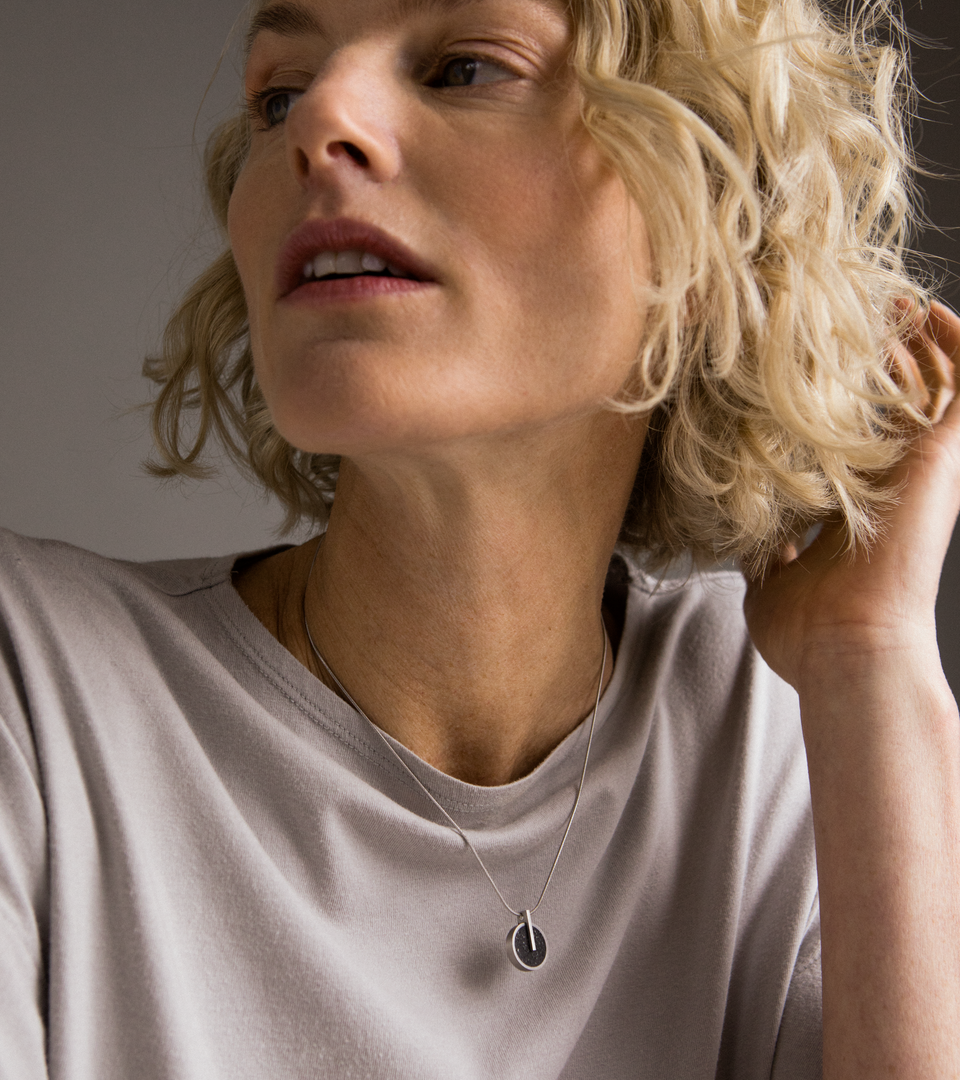 Model wearing Memento Eternal pendent with black concrete set into small circular stainless steel design.