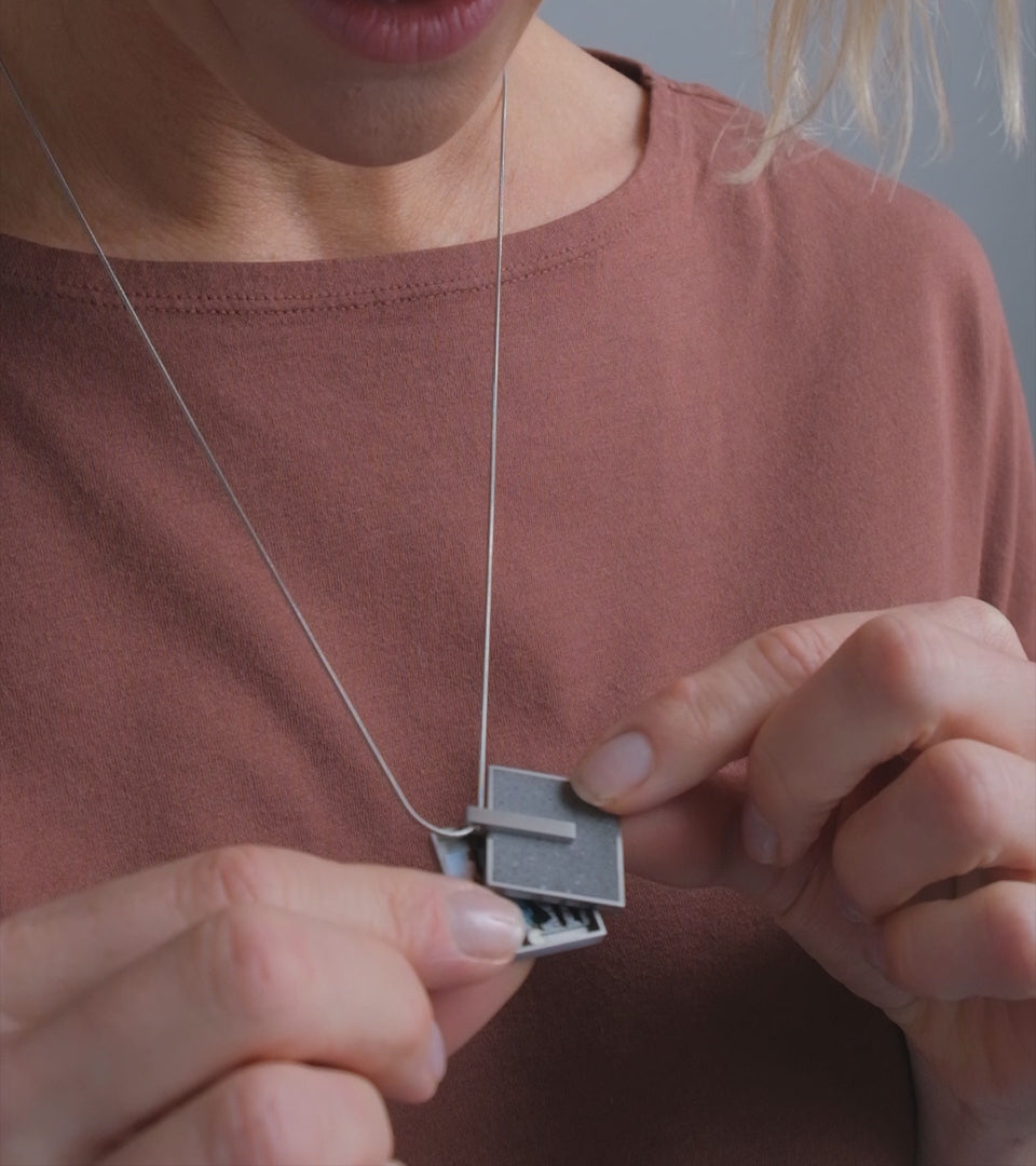Video of model wearing Memento Mindful locket set with diamond dust concrete into a square stainless framework.