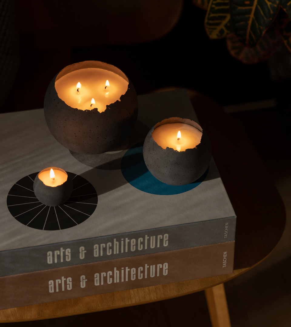 Three sizes of charcoal concrete candles sit on top of Arts & Architecture coffee table books and classic Eames molded plywood chair.