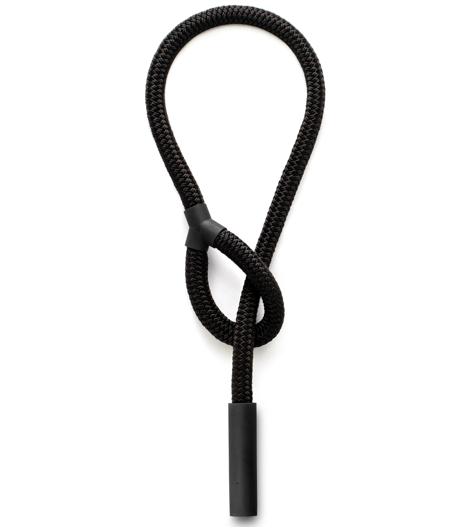 A black concrete cylinder threads through the loop of a black rope to form a unique necklace.