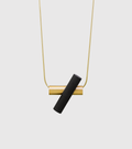 Unity+ necklace with solid 14k gold tube and chain connected to intersecting black concrete cylinder.