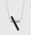 A contemporary necklace design characterized by a black concrete cylinder juxtaposed to a brushed stainless steel tube and snake chain.