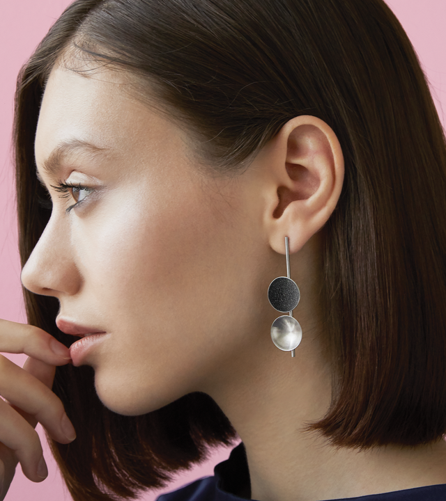 Close-up of Bauhaus inspired Freya earrings feature two double stainless steel domes, one lined with diamond dust infused black concrete both architecturally supported an elegant hanging steel post.