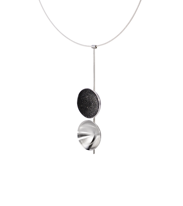 Side view of the Freya statement necklace featuring two double stainless steel larger domes, one lined with diamond dust infused black concrete both architecturally supported an elegant hanging steel post.
