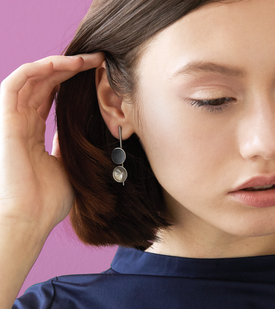 Close-up of Bauhaus inspired Freya Minor earrings feature two smaller double stainless steel domes, one lined with diamond dust infused black concrete both architecturally supported an elegant hanging steel post.