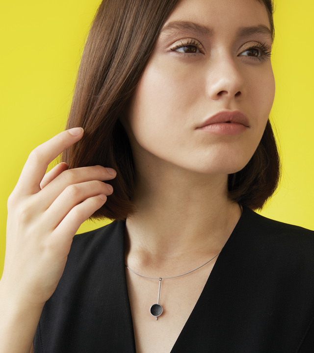 Inspira Minor minimalist necklace sparkle with diamond dust and black concrete set into a stainless steel dome suspended on top of an elegant steel post. 