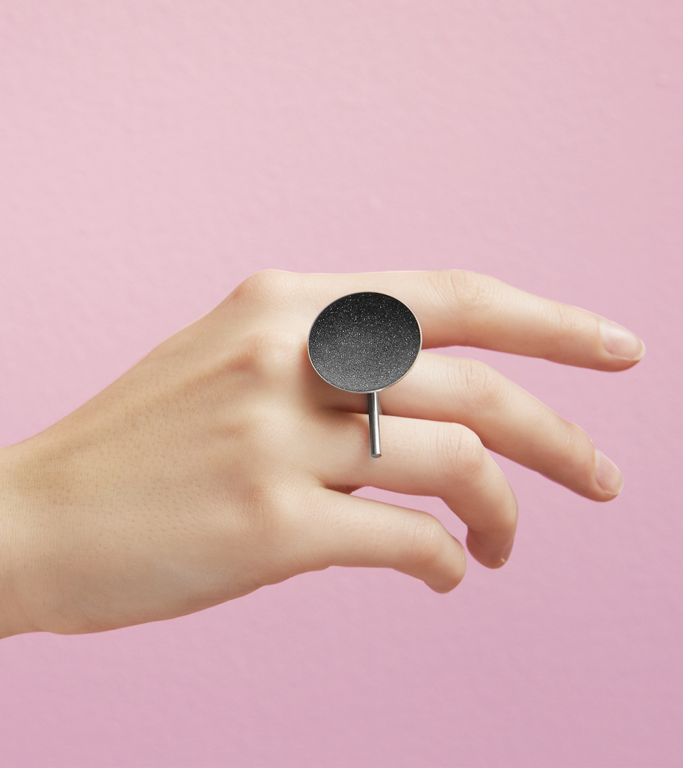 The Juno Major statement ring is features diamond dust infused into black concrete set into a small stainless steel dome architecturally connected to an extended horizontal post positioned onto a rounded steel frame. 