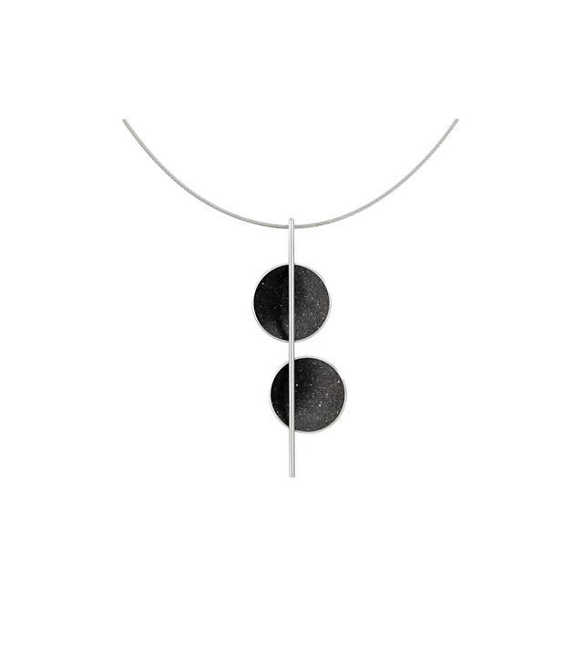 The minimalist Arago necklace sparkles with diamond dust infused black concrete set into two stainless steel domes and architecturally suspended onto an intersecting steel post and cable. 